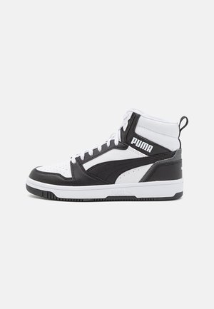 Zapatilla deportiva alta Puma en piel blanca y negra con cordones, logo de la marca en el lateral y una cinta en el talón para facilitar su uso.