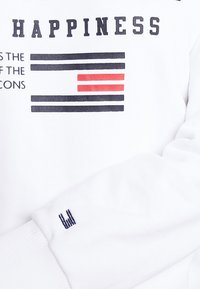 Felpa bianca con un design grafico recante la parola "HAPPINESS" e strisce orizzontali in nero e rosso. Dettagli notevoli sui polsini.