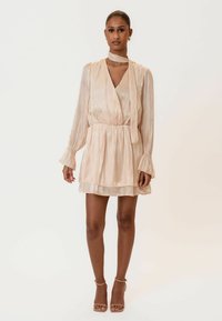 Svijetlosmeđa plisirana haljina s dugim rukavima, remenom u struku i odgovarajućim maramom za vrat. Ima blagi sjaj i slojevitu suknju.