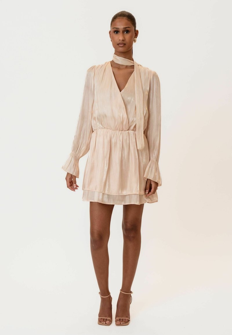 Svijetlosmeđa plisirana haljina s dugim rukavima, remenom u struku i odgovarajućim maramom za vrat. Ima blagi sjaj i slojevitu suknju.