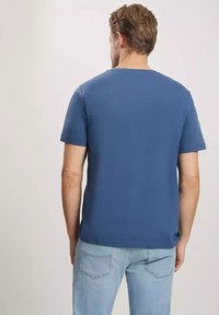 Niebieska koszulka z krótkim rękawem, wykonana z bawełny, z okrągłym dekoltem i luźnym krojem, zestawiona z jasnoniebieskimi dżinsami w luźnym stylu.