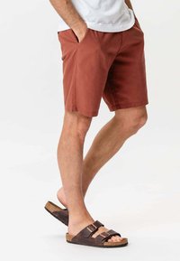 Rustfarvede shorts lavet af bomuld, med to sidelommer, i lige snit og med kant. Parret med brune sandaler med dobbelt rem.