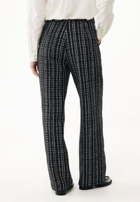 Tweed byxor med utsvängda ben i mörk marinblå botten och vit rutmönster, med en texturerad finish och smal midja, ihop med svarta skor.