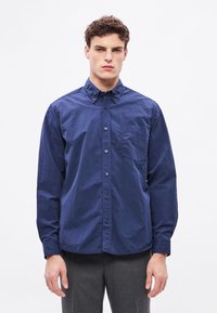 Cămașă bleumarin cu nasturi, realizată din bumbac, cu buzunar frontal, guler clasic și mâneci lungi cu manșete cu nasturi.