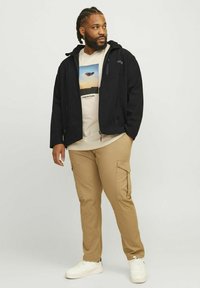 Zwart zip-up jack met een capuchon, crèmekleurig graphic t-shirt, khaki cargo broeken en witte sneakers. Gladde stof en een relaxte pasvorm.