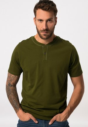 Camiseta de manga corta verde oliva con escote tipo henley. Presenta una tapeta de dos botones, tejido suave y corte ajustado, combinada con vaqueros azules.
