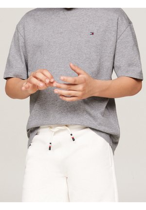 Graues Baumwoll-T-Shirt mit kurzen Ärmeln, das mit einem kleinen Markenlogo versehen ist. Kombiniert mit weißen Jogginghosen mit Kordelzug und Akzentdetails.