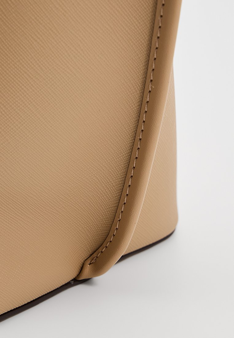 Ingrandimento di un angolo in pelle beige texture con cuciture dettagliate e bordo arrotondato liscio su uno sfondo bianco pulito.