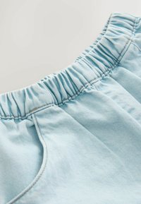 Material bleu deschis, la talie adunat, cu o textură subtilă și detalii vizibile de cusături. Prezintă o deschidere pentru buzunar pe lateral.