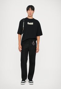 Juodas per didelis T-shirt su "GmbH" logo, derinamas su juodomis tekstūruotomis kelnėmis. Balti ir juodi sportbačiai. Maža aksesuaras ant juosmens.