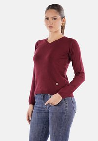 Maglione bordeaux a maniche lunghe con scollo a V, dal design aderente e un piccolo logo in versione spilla vicino all'orlo, realizzato in un tessuto a maglia testurizzato.