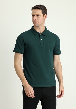 Camisa polo verde oscuro, de mangas cortas, cuello clásico, con tapeta de dos botones, material de algodón, textura suave, combinada con pantalones negros.