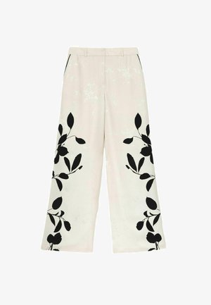 Cream wide-leg trousers with black floral leaf patterns on lower legs, side pockets, and belt loops at the waist.