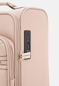 Valigia rigida beige con finitura testurizzata, dettagli in oro per la cerniera, lucchetto a combinazione e accenti del logo su cerniere e tastiera.