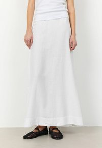 Witte linnen maxi-skirt met een vloeiende silhoeet, voorzien van een uitgesproken zoom. Gecombineerd met zwart gehaakte flats.