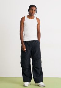 Hvid ribbet tanktop kombineret med sorte cargobukser med flere lommer og en afslappet pasform. Modellen bærer hvide sneakers.