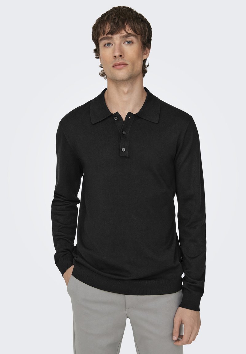 Cămașă polo neagră cu mânecă lungă, cu guler clasic, placket cu trei butoane și manșete ribbate, purtată cu pantaloni gri deschis.