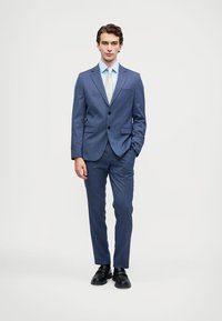 Fato com padrão xadrez azul e botões pretos, combinado com uma camisa azul clara e uma gravata prateada. O fato tem lapelas estreitas e um corte ajustado.