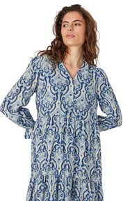 Abito a maniche lunghe in tessuto leggero con un motivo astratto blu e bianco, scollatura a V e design a gonne sovrapposte.