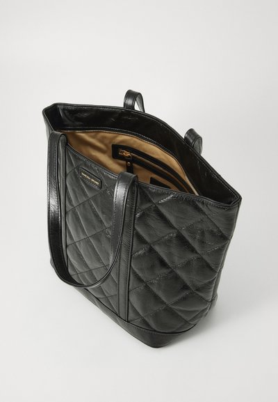 Sac fourre-tout en cuir matelassé noir avec deux poignées et un intérieur marron. Doté d'une poche zippée et d'une plaque de marque en métal sur le côté.