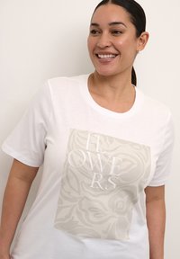 Korte mouw witte t-shirt met een grote bloemgrafiek in een gedempte tint, met het woord "BLOEMEN" in witte letters op de voorkant.