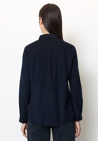 Granatowa koszula z długim rękawem, kołnierzykiem, mankietami na guziki i zakładką z tyłu. Wykonana z gładkiego materiału, z zaokrąglonym dołem.