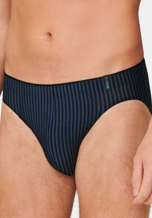 Close-up van een mannelijk torso dat zwarte slipjes met verticale blauwe strepen draagt en een klein zacht stoffen label aan de tailleband heeft.