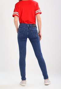 Jeans ajustados de color azul con una cintura de altura media, bolsillos traseros y un lavado sutil. Combinados con una camiseta de manga corta roja con rayas blancas.