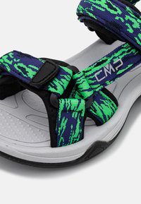 Sandalias con base negra y suela gris, que cuentan con correas de patrón verde y azul. Incluyen cierres ajustables para un ajuste seguro.