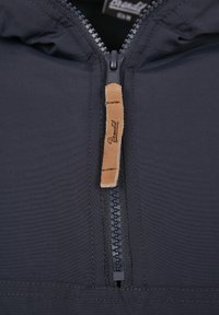 Chaqueta azul marino con un acabado texturizado, presenta un cierre central con cremallera y un tirador de cuero con marca grabada.
