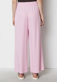 Pantaloni a gamba larga di un rosa chiaro, con vita elastica, tessuto fluido e texture liscia; presentano un orlo pulito e una vestibilità rilassata.