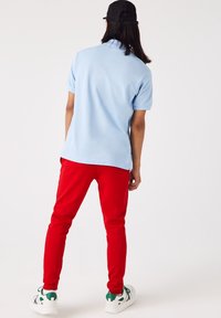 Ljusblå pikétröja tillsammans med röda tapered byxor, med en slät textur. Vita sneakers med gröna detaljer fulländar outfiten.