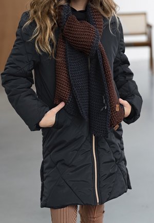 Schwarze gesteppte Jacke mit einem Reißverschluss vorne, zwei seitlichen Taschen und einem braunen sowie marineblauen gestrickten Schal. Gestreifte Hose rundet das Outfit ab.