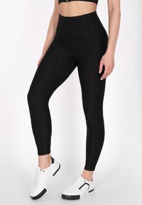 Zwarte, gestructureerde leggings met een hoge tailleband hebben een honingraatpatroon en zijn gecombineerd met witte sneakers met zwarte accenten.