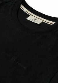Camiseta de algodón negra con cuello redondo y acabado texturizado. Presenta un pequeño logo en relieve en el pecho y un cuello interior de color contrastante.