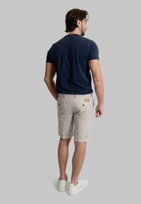 Camicia a maniche corte blu marina abbinata a pantaloni corti beige chiaro con orli arrotolati, tasche posteriori e sneakers bianche. Design e tessuto casual.