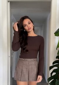 Brun genser med lange ermer kombinert med brune rutete shorts med to knapper foran. Glatt tekstur, tettsittende design og en stilig silhuett.