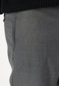 Pantaloni grigi realizzati in tessuto testurizzato, caratterizzati da una vestibilità slim e tasche laterali, con dettagli di cucitura visibili lungo le cuciture.