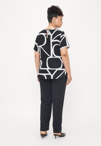 Black and white top with abstract patterns, short sleeves, and a keyhole detail at the back. Paired with black, loose-fitting pants.