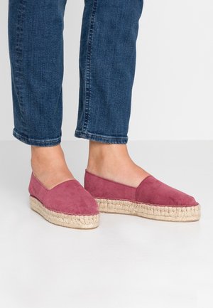 Fødder iført lyserøde suede espadrille flade sko med flettede jute-såler, parret med blå denim jeans, der er beskåret over anklerne.