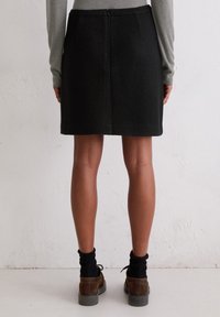 Zwarte wollen rok met een getailleerde silhouette, voorzien van een rits aan de achterkant. Draag het met een grijze lange mouwen en bruine schoeisel met zwarte sokken.