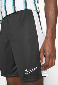 Zwarte sport shorts met een contrasterende witte zijkant, zachte stof, elastische tailleband en een witte geborduurde Nike-logo.