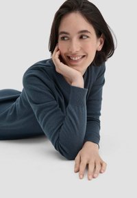 Maglione lavorato a maglia di colore blu scuro, con collo a giro e maniche lunghe. Modello sdraiato con la mano a sorreggere il mento, su uno sfondo grigio chiaro.