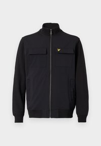 Chaqueta negra con cremallera y cuello alto, dos bolsillos en el pecho y bolsillos laterales. Presenta texturas de tela contrastantes y un pequeño logo amarillo en el pecho.