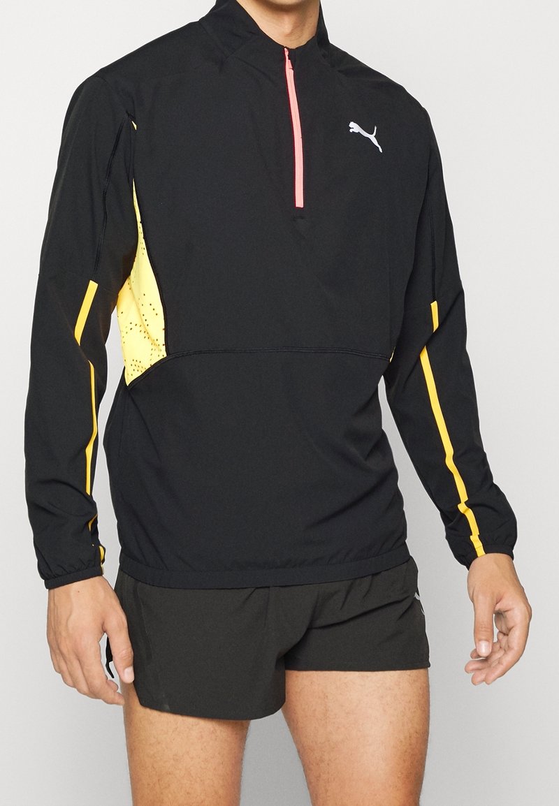 Giacca sportiva nera con pannelli gialli e una cerniera rosa, caratterizzata da un collo alto e polsini elasticizzati. Tessuto testurizzato per traspirabilità.