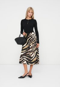 Schwarzes Langarmoberteil mit Knopfakzenten, kombiniert mit einem fließenden Rock mit einem Zebra-Streifen-Muster in Beige und Braun. Schwarze Handtasche und Schuhe.