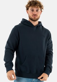 Sudadera de color azul marino hecha de un tejido suave y grueso, con un bolsillo tipo canguro en la parte frontal, puños acanalados y un logo minimalista en el pecho.
