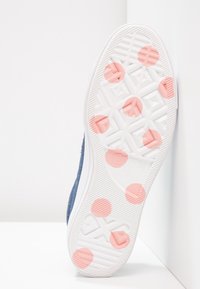 Modré semišové tenisky s bílou gumovou podrážkou, které mají texturované akcenty a růžové kruhové vzory na spodní straně.