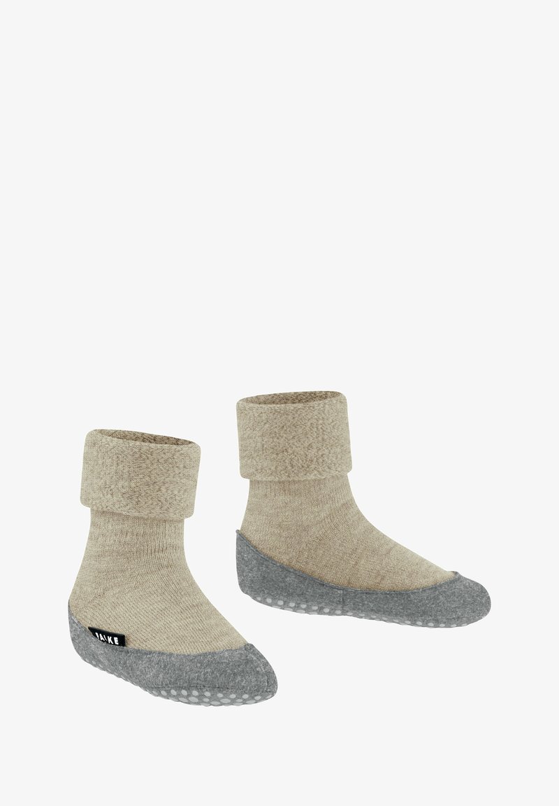 Calzini beige lavorati a maglia con risvolto e una suola grigia, texturizzata e antiscivolo, dotati di un'etichetta nera sul lato.