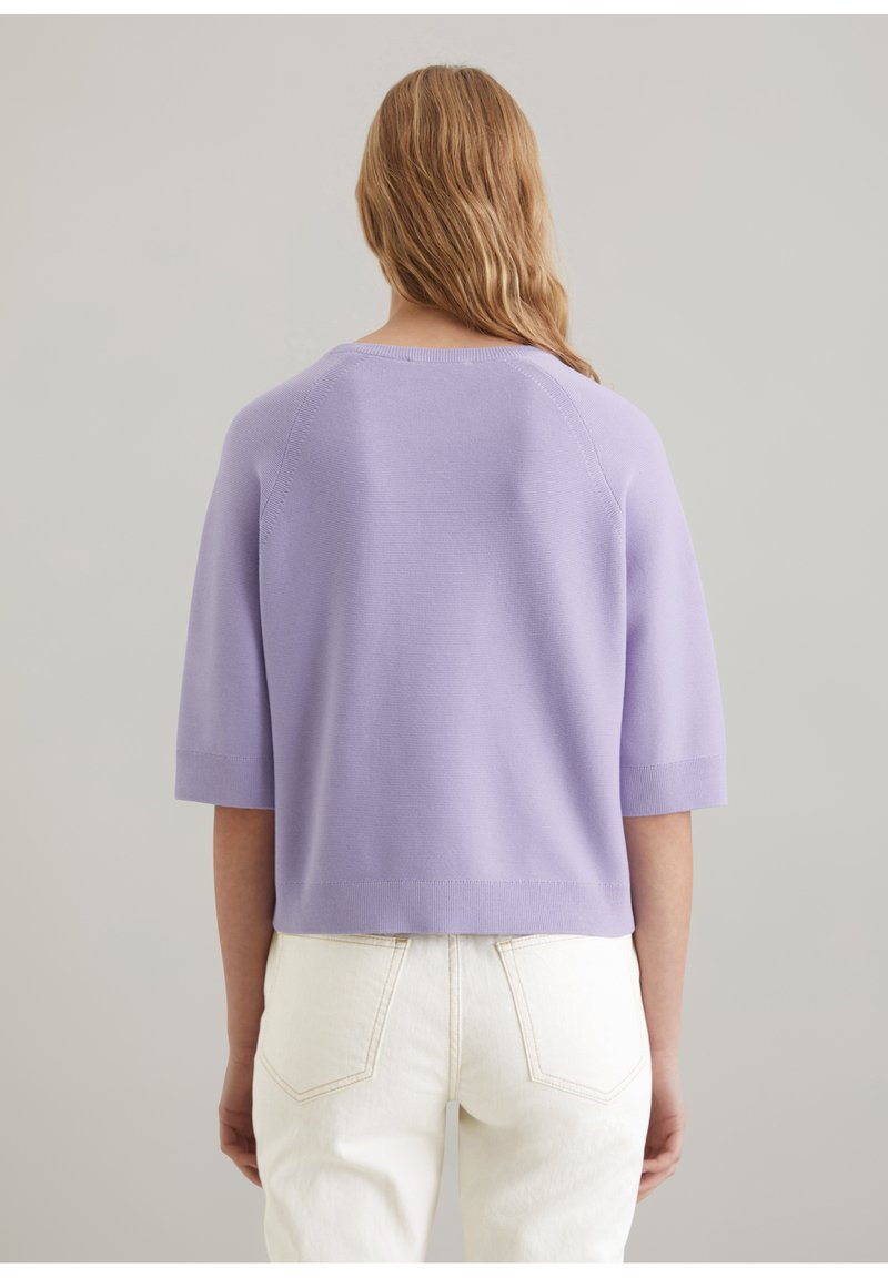 Kurzärmliges Strickoberteil in Helllila mit rundem Halsausschnitt und geripptem Saum, kombiniert mit weißen Jeans. Glatte Textur. Lässiges Design.